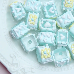 Macro view of light blue square hand-painted DIY beads with floral relief on a white tray