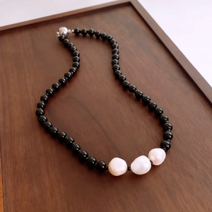 Detail of baroque pearls and black glass beads necklace on dark wooden tray