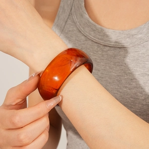 Detailed view of broad amber resin bangle featuring natural ink textures on model's wrist