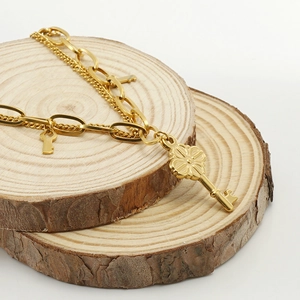 Layered gold stainless steel chain bracelet with key pendant on a rustic wood slice base