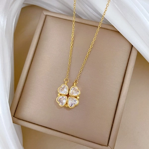 Macro detail of golden four-leaf clover necklace with heart crystals on soft white fabric