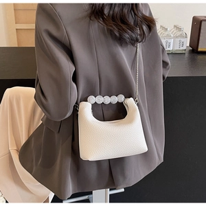Close-up of white mini dumpling bag with pearl handle and silver chain strap details