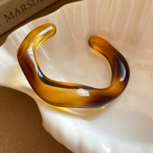 Close-up of amber wavy resin open bangle on white ceramic tray with soft light