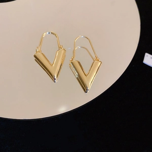 Vue macro de boucles d'oreilles dorées en forme de V se reflétant sur un miroir noir