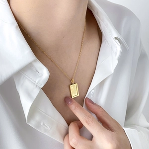 Detail shot of a golden rectangular sunburst pendant necklace worn on a white silk shirt