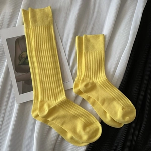 Detailed macro view of yellow cotton ribbed crew socks laid on pleated fabric background