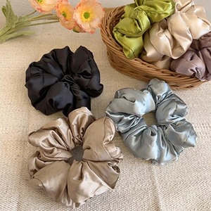 Close-up of assorted glossy silk satin scrunchies in a woven basket with flowers