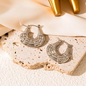 Detail of woven textured crescent hoop earrings in silver on a stone display