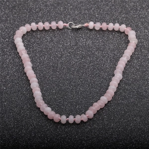 Macro detail of natural pink stone beaded necklace with silver lobster clasp on black background