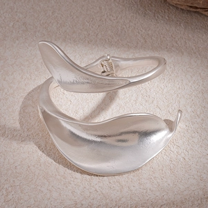 Close-up of matte silver metal cuff bracelet with organic petal shape on stone surface