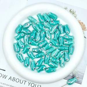 Detail of glossy teal ceramic fish beads for handmade DIY jewelry in a white porcelain bowl