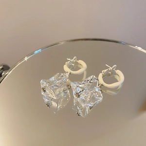 Macro detail of irregular transparent acrylic ice-cube drop earrings on mirror base