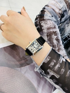 Elegant rectangle silver watch with roman numerals on model wrist with magazine background
