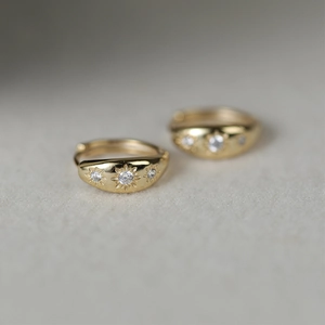Detail of gold huggie earrings with sparkling starburst-set zircons on soft velvet