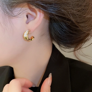 Close-up of golden C-shaped earring with white pearls and olive green gemstone on model