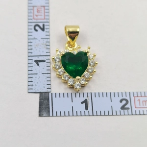 Detail of green heart pendant with gold base and zircon stones next to a measuring ruler