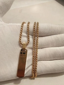 Detailed view of a gold-plated 3D rectangular pendant on a box chain held in hands