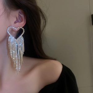 Close-up of sparkling rhinestone heart tassel earrings worn by a female model