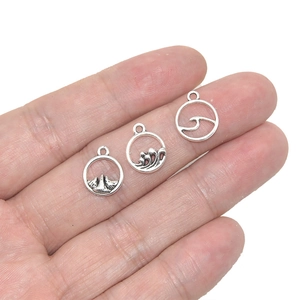 Three antique silver round pendants with mountain and wave designs held in hand for scale
