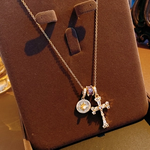 Detail of 18k gold cross necklace with zircon starburst and purple bead on velvet stand