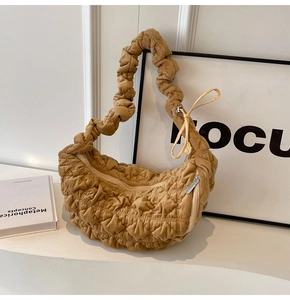 Detail of quilted croissant bag in warm khaki with pleated strap on a white surface