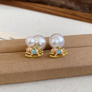 Close-up of pearl stud earrings with a colorful rocking horse pendant on soft velvet