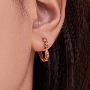 Golden hoop earring with colorful zircon heart details worn on ear by a model