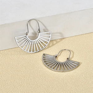 Détail de boucles d'oreilles évidées argentées en forme d'éventail sur fond beige