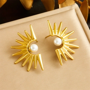 Golden sunburst earrings with white pearl centers displayed on a beige cushion
