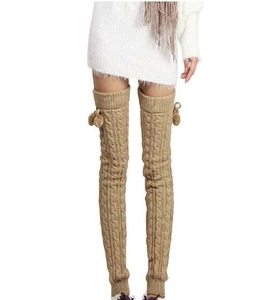 Detail of cable knit thigh high leg warmers in light brown with decorative pom poms