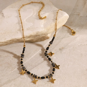 Golden stainless steel necklace with black beads and star pendants on a beige stone