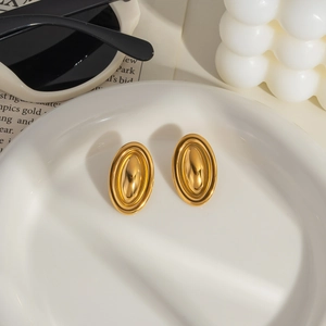 Detail of gold layered oval stud earrings on ceramic tray with elegant lifestyle props