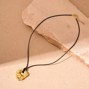 Detail of a gold irregular geometric metal pendant on a black cord over a stone surface