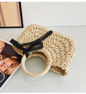 Close-up of woven straw handbag with elegant black lace bow on a minimal surface