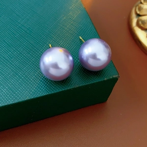 Detailed macro view of purple pearl stud earrings with gold pins on a green gift box