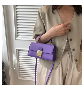 Detail of purple crossbody bag with golden metal clasp held by model in neutral setting