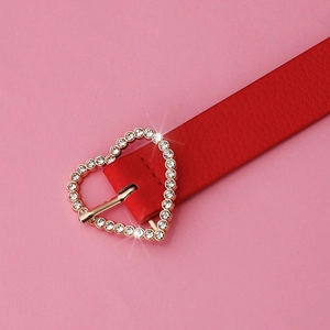 Close-up of red leather belt featuring a golden heart-shaped buckle with sparkling rhinestones