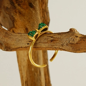 Minimalist adjustable gold ring with green rhinestone bow on natural wood stand