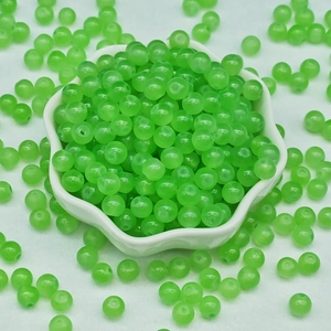 Macro view of transparent green chalcedony beads in a white petal ceramic bowl