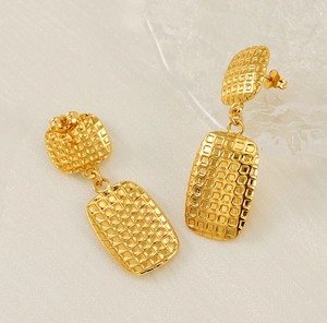 Close-up of golden geometric square earrings with textured checkered pattern on white fabric