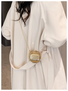 Close-up of golden metallic ripple mini bag with chain strap on beige winter coat