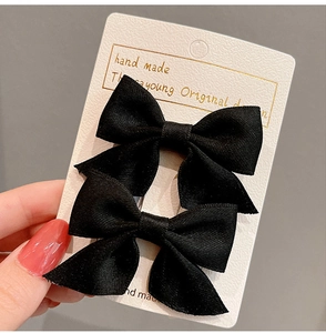 Detail of two black matte fabric bow hair clips with twill texture on display card