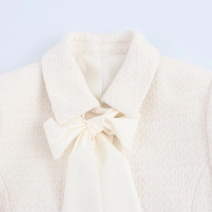 Détail du col d'une veste en tweed crème avec un nœud élégant en texture soie