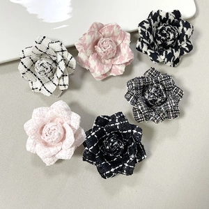 Detailed view of tweed camellia brooches in houndstooth and solid colors on beige fabric