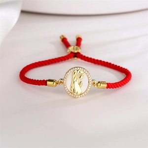 Macro shot of red braided rope bracelet with a gold religious portrait pendant and white stones