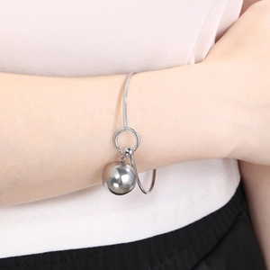 Detail of a minimalist silver bangle featuring a hollow spherical charm worn on the wrist