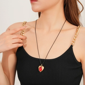Close-up of a vintage golden heart pendant with a red gemstone on a black cord necklace