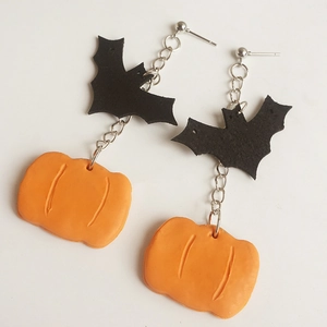 Detailed view of Halloween earrings featuring black bats and orange pumpkins on white background