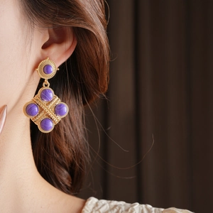 Dettaglio di orecchini vintage dorati con gemme viola e pendenti a forma di rombo