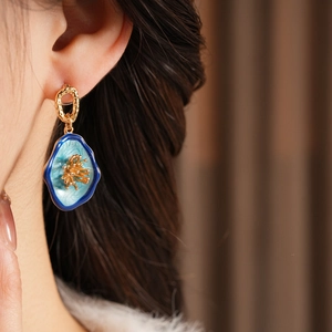 Close-up detail of vintage floral gold earrings with blue enamel petals on a female model